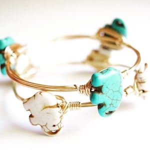 May include: A gold wire bracelet with turquoise and white elephant charms. The bracelet is double-stranded and has a delicate, feminine look.