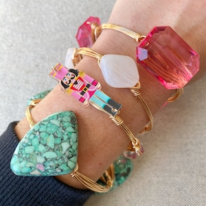 May include: A set of four gold wire wrapped bracelets with different charms. The charms include a turquoise stone, a white stone, a pink stone, and a nutcracker figurine.