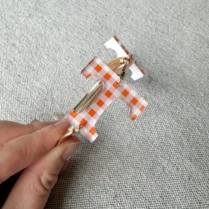 Op de afbeelding: Twee gouden draad armbanden met oranje en wit geruit patroon hars. De armbanden zijn op elkaar gestapeld.