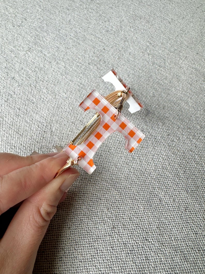 Op de afbeelding: Twee gouden draad armbanden met oranje en wit geruit patroon hars. De armbanden zijn op elkaar gestapeld.