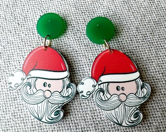 May include: A pair of Christmas-themed earrings featuring a cartoon Santa Claus face with a white beard and moustache, red hat, and green circular accents.
