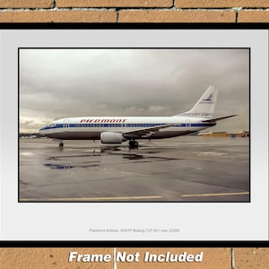Puede incluir: Un avión Boeing 737-301 de Piedmont Airlines con el número de registro N301TP. El avión está estacionado en una plataforma con un cielo nublado en el fondo. El avión está pintado en un esquema de colores blanco, azul y rojo con el logotipo de Piedmont Airlines en el lateral.