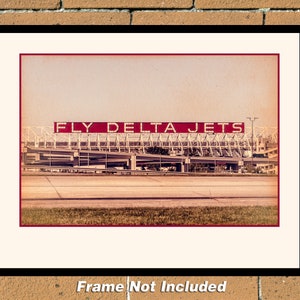 May include: A vintage-style photograph of a large red sign that reads "FLY DELTA JETS" above a large airport terminal building. The photo has a faded, sepia tone.
