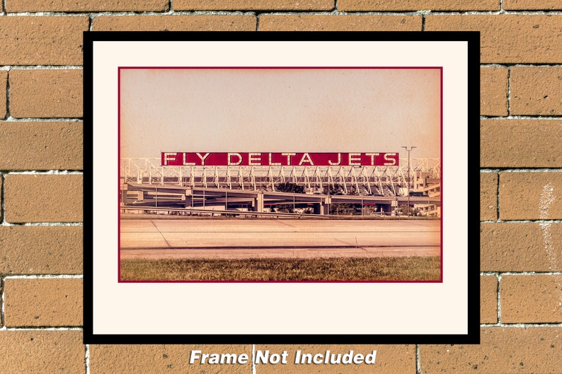 May include: A vintage-style photograph of a large red sign that reads "FLY DELTA JETS" above a large airport terminal building. The photo has a faded, sepia tone.