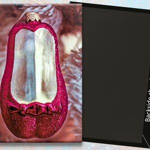 May include: A glittery red Christmas ornament shaped like a penguin, with a white and silver interior. The ornament has a gold-colored cap and is hanging on a white Christmas tree. The backside of the magnet is black.