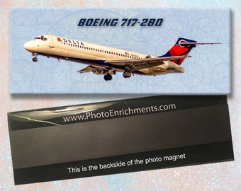 Op de afbeelding: Een fotomagneet met een wit, blauw en rood Delta Airlines Boeing 717-280 vliegtuig tegen een lichtblauwe achtergrond. De tekst "BOEING 717-280" is in zwart gedrukt bovenaan de magneet. De tekst "www.PhotoEnrichments.com" is in wit gedrukt op een zwarte achtergrond onderaan de magneet. De tekst "This is the backside of the photo magnet" is in wit gedrukt op een zwarte achtergrond onderaan de magneet.