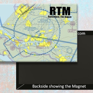 Puede incluir: Un imán con un mapa azul y blanco del aeropuerto de Róterdam, La Haya, con el código de aeropuerto RTM y el texto "Rotterdam, La Haya" impreso en el imán. El imán es negro y tiene el texto "com" y "Backside showing the Magnet" impreso en él.
