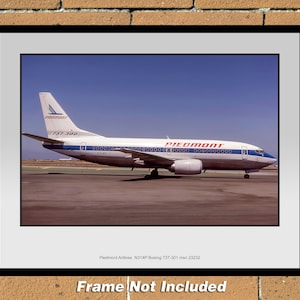 Puede incluir: Una impresión enmarcada de un avión Boeing 737-300 de Piedmont Airlines en una pista. El avión es blanco con detalles en azul y rojo. El texto "Piedmont" es visible en el fuselaje y la cola del avión. Las palabras "Frame Not Included" están en la parte inferior.