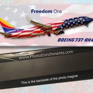 Pode incluir: Um íman retangular com um avião Boeing 737-8H4 com um design patriótico. O avião é pintado com as cores vermelho, branco e azul, com as palavras "Freedom One" acima. A parte de trás do íman é visível, com o texto "This is the backside of the photo magnet."