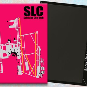 May include: A pink magnet featuring a white outline of the Salt Lake City International Airport (SLC) layout. The text "SLC Salt Lake City, Utah" is printed in black at the top of the magnet.