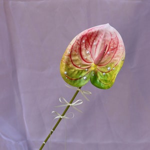 Pink and green faux anthurium with bows tied to the stem and pearls hand placed onto the flower and stamen.