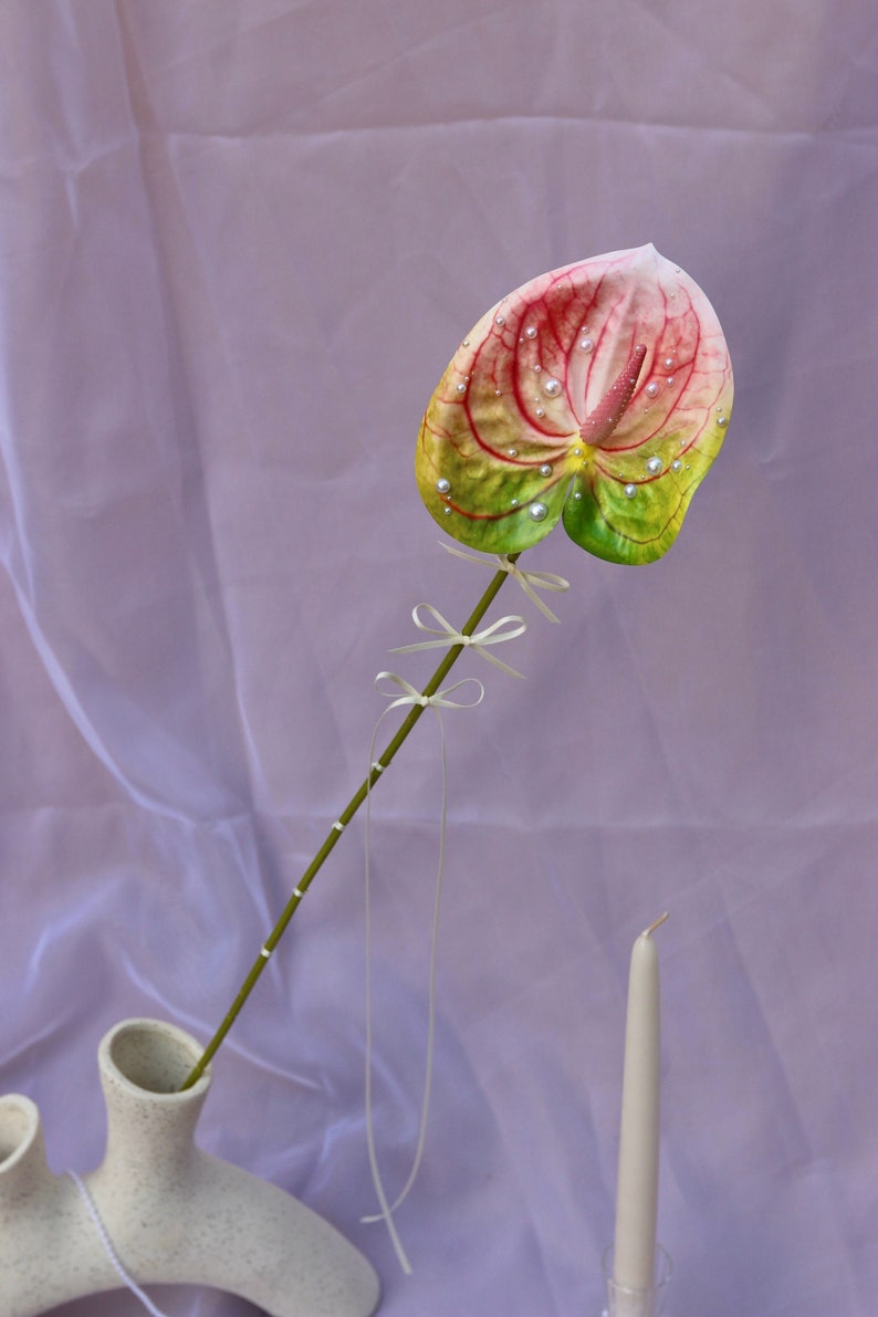 Pink and green faux anthurium with bows tied to the stem and pearls hand placed onto the flower and stamen.