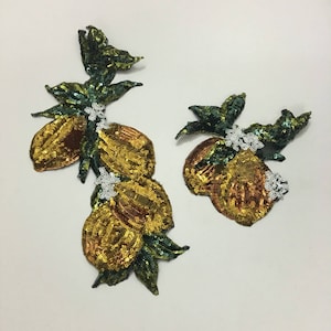May include: Two gold and green sequined lemon patches with white flower accents. The larger patch has three lemons and the smaller patch has two lemons.