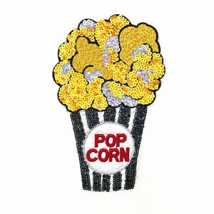 May include: A yellow and white popcorn patch with sequins. The popcorn is in a black and white striped container with the word "POP CORN" in red letters.