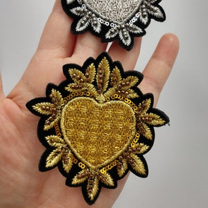 Op de afbeelding: Twee geborduurde hartpatches, een gouden en een zilveren, met een zwarte fluwelen achterkant en pareldetails.