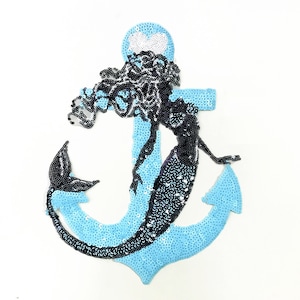 Puede incluir: Un parche de plancha de lentejuelas azul y negro con una sirena de pelo largo envuelta alrededor de un ancla.