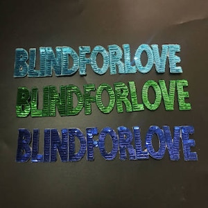 May include: Three versions of the phrase "Blind For Love" in blue, green, and dark blue sequins.