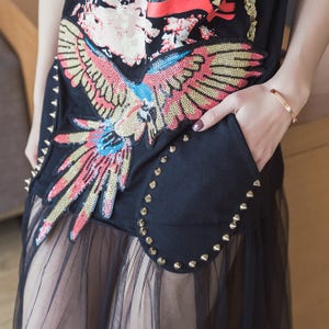 May include: Black t-shirt with a colorful embroidered parrot design and gold studs. The shirt is layered over a sheer black tulle skirt.