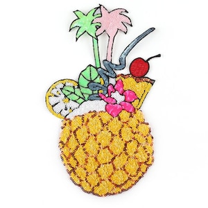 May include: A yellow pineapple with green leaves and a pink flower on top. There is a red cherry and a green lime on the side. The pineapple is made of sequins.