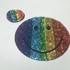 May include: Two rainbow sequin smiley face patches. The larger patch is about 10 cm in diameter and the smaller patch is about 5 cm in diameter.