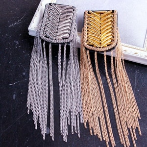 May include: Two decorative brooches with a chain fringe. The brooch on the left has a silver finish and the brooch on the right has a gold finish.