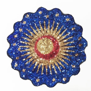 Può includere: Applicazione rotonda di paillettes con bordo smerlato. Il design presenta un cerchio centrale dorato, un anello rosso e raggi dorati. L'esterno è blu con paillettes dorate sparse.