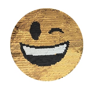 Puede incluir: Una almohada reversible de lentejuelas doradas con una cara sonriente negra y blanca guiñando un ojo en un lado y una superficie de lentejuelas doradas en el otro lado.