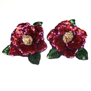 May include: Two red and pink sequined flower patches with green leaves. The flowers have a gold center.