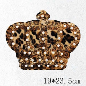 Könnte beinhalten: Ein gold- und brauner kronenförmiger Patch mit Leopardenmuster und weißen Perlenverzierungen. Der Patch misst 19 x 23,5 Zentimeter.