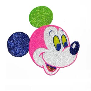 Può includere: Toppa con il volto di Topolino con paillettes. La testa è rosa, il viso bianco e il naso blu. Le orecchie sono blu e verdi. Gli occhi sono gialli e blu. La bocca sorride con una lingua dorata con paillettes.