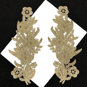 May include: Two gold glitter floral appliques with a delicate lace design. The appliques are perfect for adding a touch of sparkle and elegance to any project.