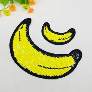 May include: Two yellow banana-shaped patches made of sequins with black outlines. The larger banana is curved and the smaller banana is a crescent shape.
