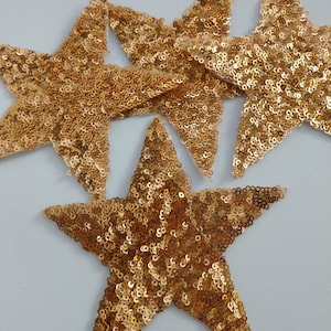 Può includere: Quattro paillettes dorate a forma di stella, ciascuna con una finitura lucida e scintillante. Le paillettes sono perfette per aggiungere un tocco di glamour a qualsiasi progetto artigianale.