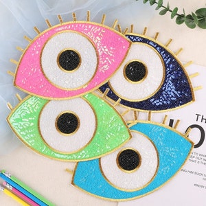 May include: Four colourful evil eye patches with white centres and gold trim. The patches are made of sequins and beads.