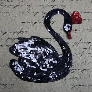 May include: Black sequin swan applique with a red sequin crown. The swan is facing right and has a white outline.
