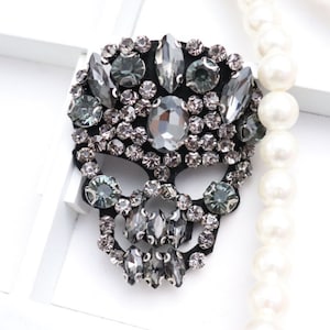 Op de afbeelding: Een zwarte schedelvormige patch bedekt met heldere en grijze strass steentjes. De patch is ongeveer 7,5 cm breed en 5 cm hoog.