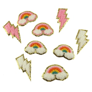 以下が含まれることがあります： 虹と稲妻をあしらった刺繍パッチのコレクション。虹には白い雲があり、稲妻はピンクと白です。すべてのパッチには金色のグリッターの縁取りがあります。
