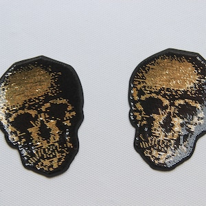 Puede incluir: Dos parches de calavera negros y dorados con un acabado brillante.