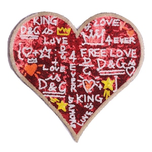 Può includere: Toppa a forma di cuore rosso con contorno dorato e paillettes. La toppa è ricoperta di scritte bianche in stile graffiti che dicono "KING", "D&G", "LOVE", "M14EVER", "FREE LOVE", "D&G", e "KING".