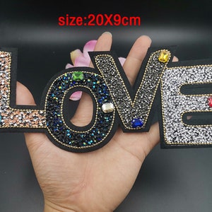 May include: A black felt patch with the word "LOVE" spelled out in rhinestones. The patch is 20 by 9 centimeters and features a variety of colored rhinestones.