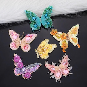 May include: Six colourful butterfly-shaped embellishments with sequins and beads. The butterflies are in shades of blue, pink, yellow, and orange.
