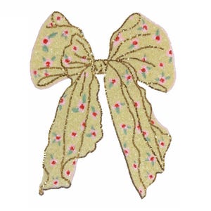 May include: A large, decorative bow with a light yellow background, covered in sequins and small pink and red floral patterns. The bow is outlined with gold sequins.