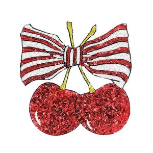 Könnte beinhalten: Ein paillettenbesetzter Aufnäher mit einem Paar roter Kirschen mit grünen Stielen und einer rot-weiß gestreiften Schleife. Die Kirschen und die Schleife sind mit Pailletten verziert, was einen funkelnden Effekt erzeugt. Der Aufnäher befindet sich auf weißem Hintergrund.