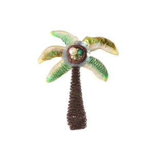 Op de afbeelding: Een palmboom broche met een stam omwikkeld met donkerbruin draad. De palmbladeren zijn gemaakt van iriserende groene en gouden lovertjes. Het midden van de boom is versierd met een cluster van witte, groene en gouden kralen en kleine kristallen.