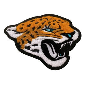 Op de afbeelding: Een close-up van een geborduurde patch met een brullende jaguar kop met oranje en zwart bont. De ogen van de jaguar zijn blauw en de bek is open, met scherpe tanden zichtbaar.