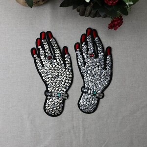May include: Two black fabric patches with a design of hands covered in silver sequins. The hands have red nail polish and red and green gem accents.