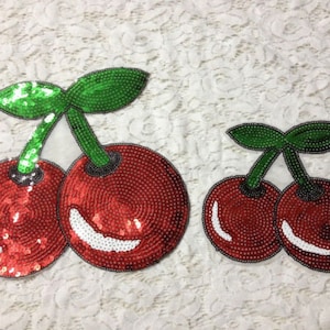 Puede incluir: Dos parches en forma de cereza roja y verde hechos de lentejuelas. El parche de cereza más grande tiene dos cerezas, mientras que el parche más pequeño tiene una.