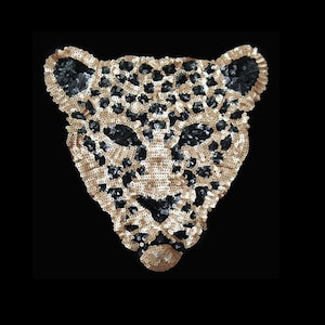 Puede incluir: Una aplicación de cara de leopardo de lentejuelas doradas y negras. La aplicación está hecha de pequeñas lentejuelas redondas que se cosen juntas para crear un diseño detallado.