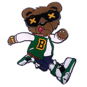 May include: A brown bear wearing green and white clothing, sunglasses with an 'X' pattern, and a gold bracelet. The bear is jumping and has its tongue sticking out. The bear is wearing a green varsity jacket with a yellow 'B' on the front.