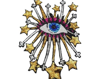 Könnte beinhalten: Ein großes, farbenfrohes Auge mit blauer Iris und rosa Augenlidern, umgeben von goldenen und silbernen Pailletten in Form von Sternen.
